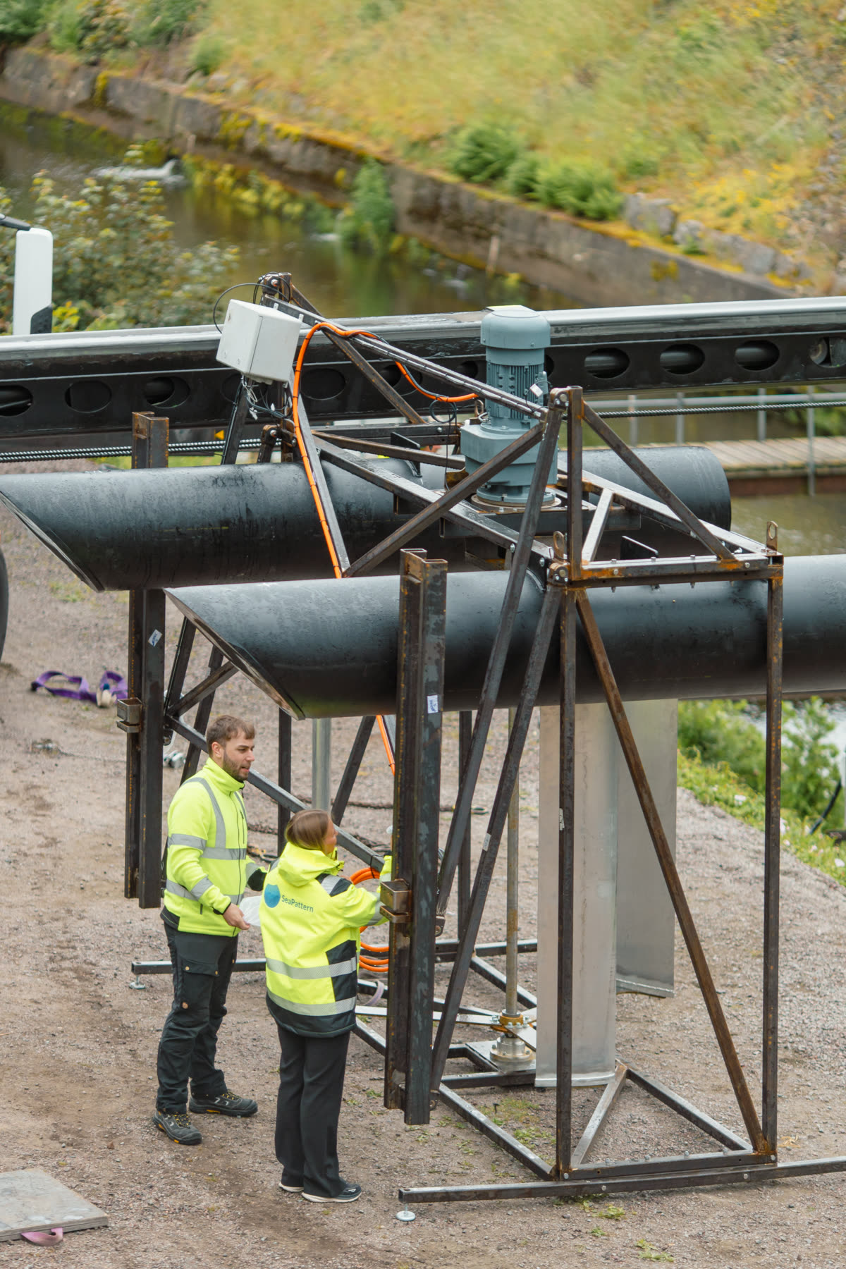 Two SeaPattern technicians working on a turbine frame beside the canal